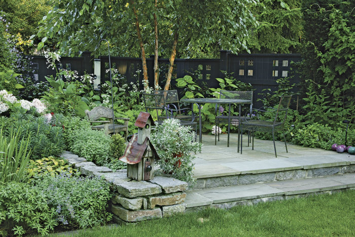 Table and chairs on a floating patio built from scratch with weathered stones, surrounded by plants with a black fence at the back