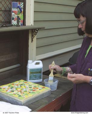 woman ready to apply sealer to the mosaic surface outdoors with a small paintbrush